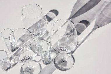 Boş şarap kadehleri ve bardaklar. Soyut gölgeler, güneş ışığı, beyaz arkaplan, yakın plan.