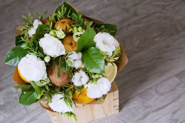 Bouquet of fruits and flowers. Coconut, brown pear, orange, lemon, kiwi fruit, cotton, pistachio, salal, white eustoma. Gray wooden background.