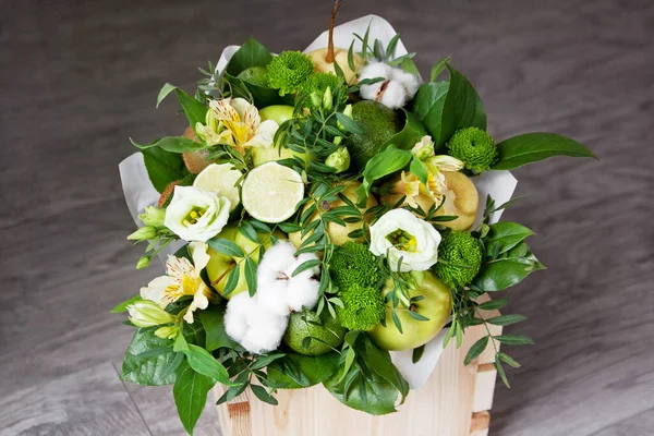 Bouquet of fruits and flowers. Asian pear, green chrysanthemum, yellow alstroemeria, avocado, cotton, pistachio, apple, lime, salal, kiwi fruit. Gray wooden background.