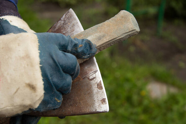 A man in gloves sharpens an iron axe with a special knife stone. A place for inscription. selective focus