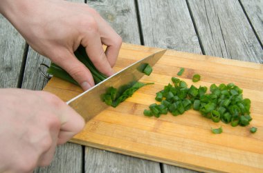 Adamın elleri yeşil soğanı tahtada bıçakla kesiyor.