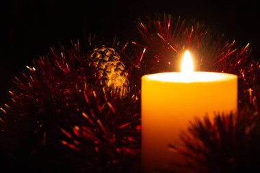 O kadar da kalın olmayan yanan mum kırmızı Noel süsleriyle çevrili duruyor. Bir yeni yıl oyuncağı yakınlarda bir tümsek şeklinde duruyor. Alçakgönüllülük. Tüm dikkatler cam oyuncağa çevrildi..