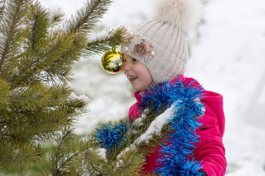 Beş yıllık mutlu bir kız, burnunu kışın sokağın dalında asılı duran sarı camdan bir Noel oyuncağına yasladı. Ağacı yeni yıl için mavi süslemeler ve oyuncaklarla süslüyor.