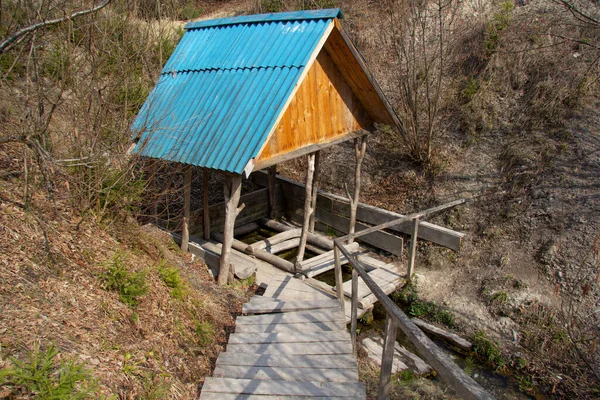 A wooden well in the forest above a source of clean water. A creek runs out of it. A wooden staircase leads to the spring — Stock Photo, Image