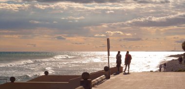 Gün batımında Sitges açıklarında ufka bakan yürüyüşçülerin siluetleri. Deniz manzarası. Garraf bölgesi, Barselona, Katalonya, İspanya.