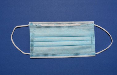 Tek kullanımlık 3 kat cerrahi olmayan yüz maskesi ve mavi arka planda izole edilmiş elastik kulak halkaları.