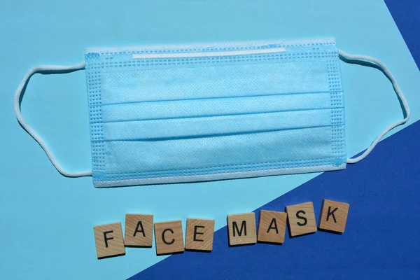 Face Mask in 3D wooden alphabet letters and a disposable 3ply non-surgical face mask with elastic loops isolated on blue background