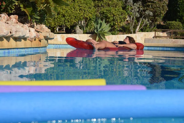 Yazın yüzme havuzunda yüzen genç bir kadın ve ön planda yüzen erişteler.