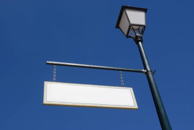 Mavi gökyüzüne karşı lamba direğinden sarkan eski moda boş tabela. 