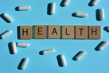 Sağlık, 3 boyutlu tahta alfabe harfleri ve mavi arka planda beyaz kapsüller.