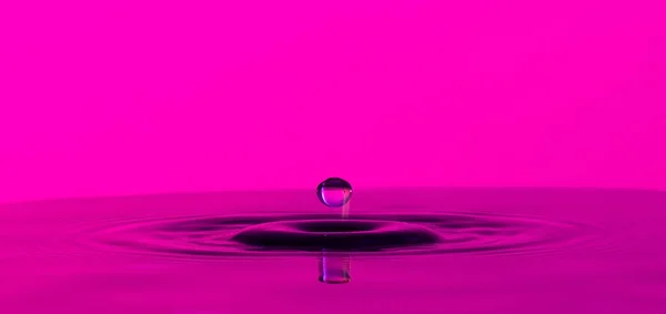 Drop of liquid splashing on quiet surface on a color background