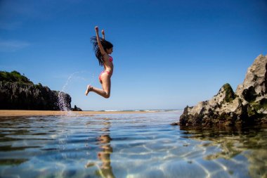 Pik bikinili kız plajda atlıyor.