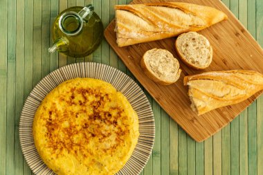 Kırsal bir tabakta İspanyol tortilla, cam bir kavanoz zeytinyağı ve üzerinde biraz ekmek ve ahşap bir masa örtüsü.