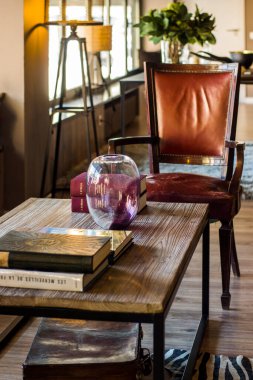 Oturma odasında kitap ve deri sandalye olan eski ahşap masa.