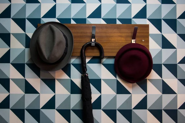 Coat rack with some hats and an umbrella on a blue triangles wall