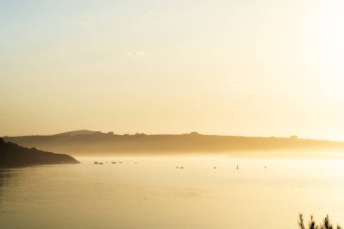 Gün batımında sisli nehir manzarası. Gün bitmeden önce bazı insanlar su sporları yapıyor.