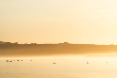 Gün batımında sisli nehir manzarası. Gün bitmeden önce bazı insanlar su sporları yapıyor.