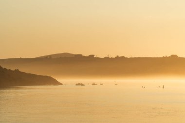 Gün batımında sisli nehir manzarası. Gün bitmeden önce bazı insanlar su sporları yapıyor.