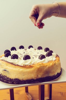 Kremalı kekin üzerine beyaz arka planda siyah bisküvi serpiştiren bir el görüntüsü