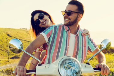 Taze elbiseli birkaç genç arkadaş gün batımında sahilde motosikletle eğleniyor ve gülümsüyorlar.