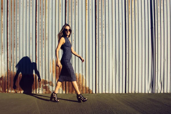 Female young model walking with a long dress in an industrial area with a rusty fence on the background