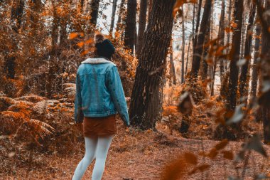 Sonbahar renklerinde bir ormanda mevsim kıyafetleriyle yürüyen genç bir kadın.