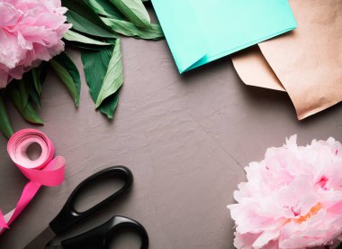 Çiçekçi dükkanı için düz yatıyordu. Pembe şakayıklar, kurdele, makas, el işi kağıt, zarf gri arka planda düzenlenir..