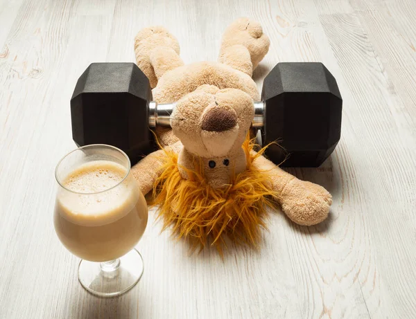 Fitness concept - sports and fitness at home - tired stuffed toy under hexagon dumbbell and coffee, horizontal orientation