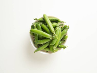 Beyaz bir masada beyaz bir kasede yeşil bezelye kabukları.