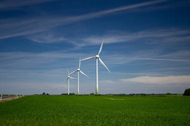 Enerji - mavi gökyüzüne karşı yeşil alanlarda üç rüzgar türbini.