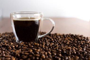 Kahveli bir fincan, ahşap bir masada, dağınık kahve çekirdeklerinin yanında duruyor..