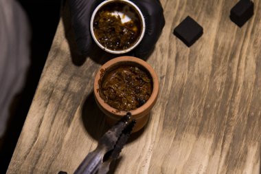 Nargile hazırlarken, bir adamın eli bir shisha kasesine meyve tütünü koyar..
