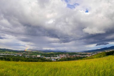 Gökkuşağı manzaralı Valasske Mezirici kasabasının manzarası. Ufuktaki tepelerde yağmur sırasında güneş manzaraya doğru parlıyor..