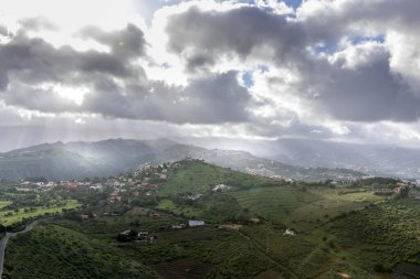 Gökyüzünde hızla hareket eden bulutlarla dolu güneşli bir günde ve çimenli toprağa yansıyan gölgelerle dolu tepeler ve vadilerle dolu engebeli engebeli bir volkan çevresindeki Gran Kanaryası doğası..