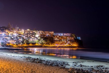 Akşamları kayalıklardaki gece şehri görüntüsü okyanus yüzeyindeki gölgelerin yansıması ve yüzeydeki sokak ışığının diğer yansımaları ile birlikte..
