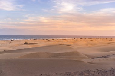 Ufuktaki okyanusa bakan kum tepeciklerinden geçen insanlar güneşli bir günde Büyük Kanarya Adası 'ndan gökyüzünde yoğun bulutlar hareket ediyor.