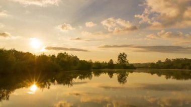 Timelapse gölünün üzerindeki gün doğumu kıyıdaki stoma hattının arkasından yükselir ve yavaş yavaş turuncu rengi gün ışığına çevirir. Hustopece Becvou Çek Cumhuriyeti su yüzeyindeki yansıması ile.