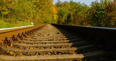 Güneşli bir günde tren raylarını emniyete alan büyük vidaların yakın görüntüsü. Yavaş bir geçitle, taşların biraz üstünden bir yan görüş geliyor..