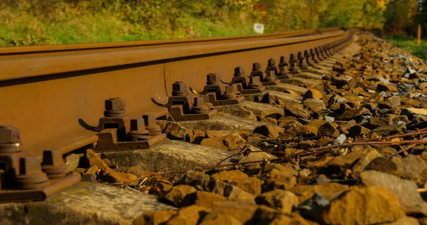 A close-up view of the large screws securing the train tracks during a sunny day with a slow passage forward with a turn from a side view from below a bit above the stones.