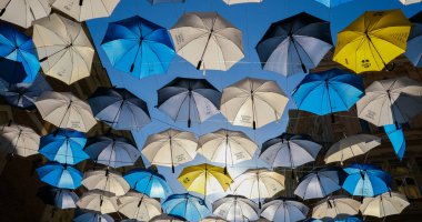 Güneşli ve rüzgarlı bir günde evlerin arasında asılı duran şemsiyeler sokağın kenarından çekilen tüm renkleri çalıyor.