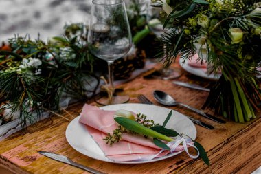 Çiçeklerle dolu eski ahşap bir düğün masası ve yiyecek için hazırlanmış bir yer. Kışın, ormanın ortasında, karla kaplı bir düğün merasimi.