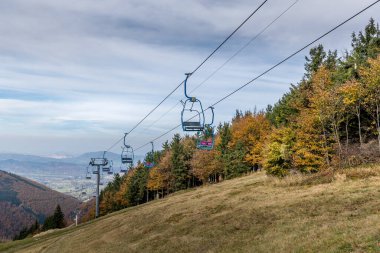Pustevny Beskids bölgesindeki manzaraya ve çevresindeki doğaya bakarken güçlü rüzgarda sallanan koltukların kış sezonu görüntüsünde kullanılan füniküler.