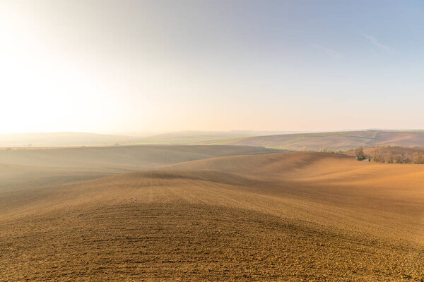 Вид на вспаханную землю после сезона в Моравийском регионе Тосканы, полный рябь с видом на деревню на заднем плане во второй половине дня солнечный день без облаков
