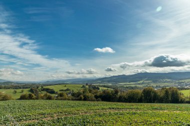 Gökyüzünde hızla hareket eden bulutlar, köye bakan güneşli bir günde ve arka plandaki yüksek tepelere ve dağlara bakan taze ekinlerle dolu bir tarladan çekildi..