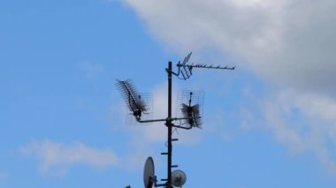 Televizyon ve internet için yüksek antenlerin zamanlaması ve evin çatısında ve arka planında hızlı hareket eden beyaz bulutlarla birlikte mavi gökyüzünde bir sürü kuş uçuşuyor..