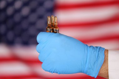 ABD 'de koronavirüs salgını. Viral Hastalık Aşısı. Amerikan bayrağının bulanık arka planında mavi eldivenli cam ampüller.