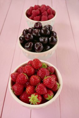 Ahududu, çilek, vişneli böğürtlen seti. Yaz meyveleri pembe pastel ahşap arka planda karışır