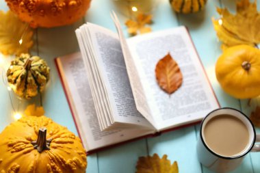 Sonbahar kitapları. Çay fincanı, açık kitap, mavi ahşap arka planda parlayan bir çelenk seti.