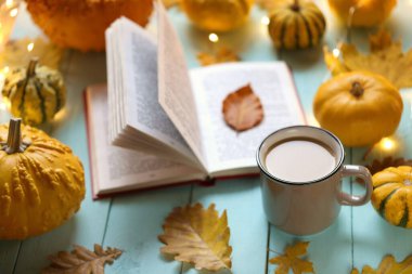 Sonbahar kitapları. Çay fincanı, açık kitap, mavi ahşap arka planda parlayan bir çelenk seti.