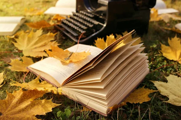 Writing Concept.Autumn Books. retro black typewriter and books with yellow maple leaves on the lawn